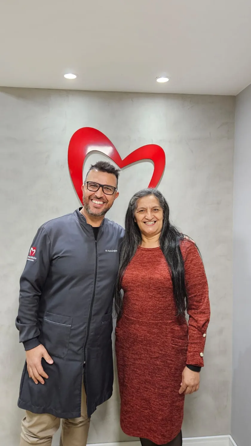 Paciente de vestido vermelho sorrindo ao lado do Dr. Marcelo Ribeiro no consultório
